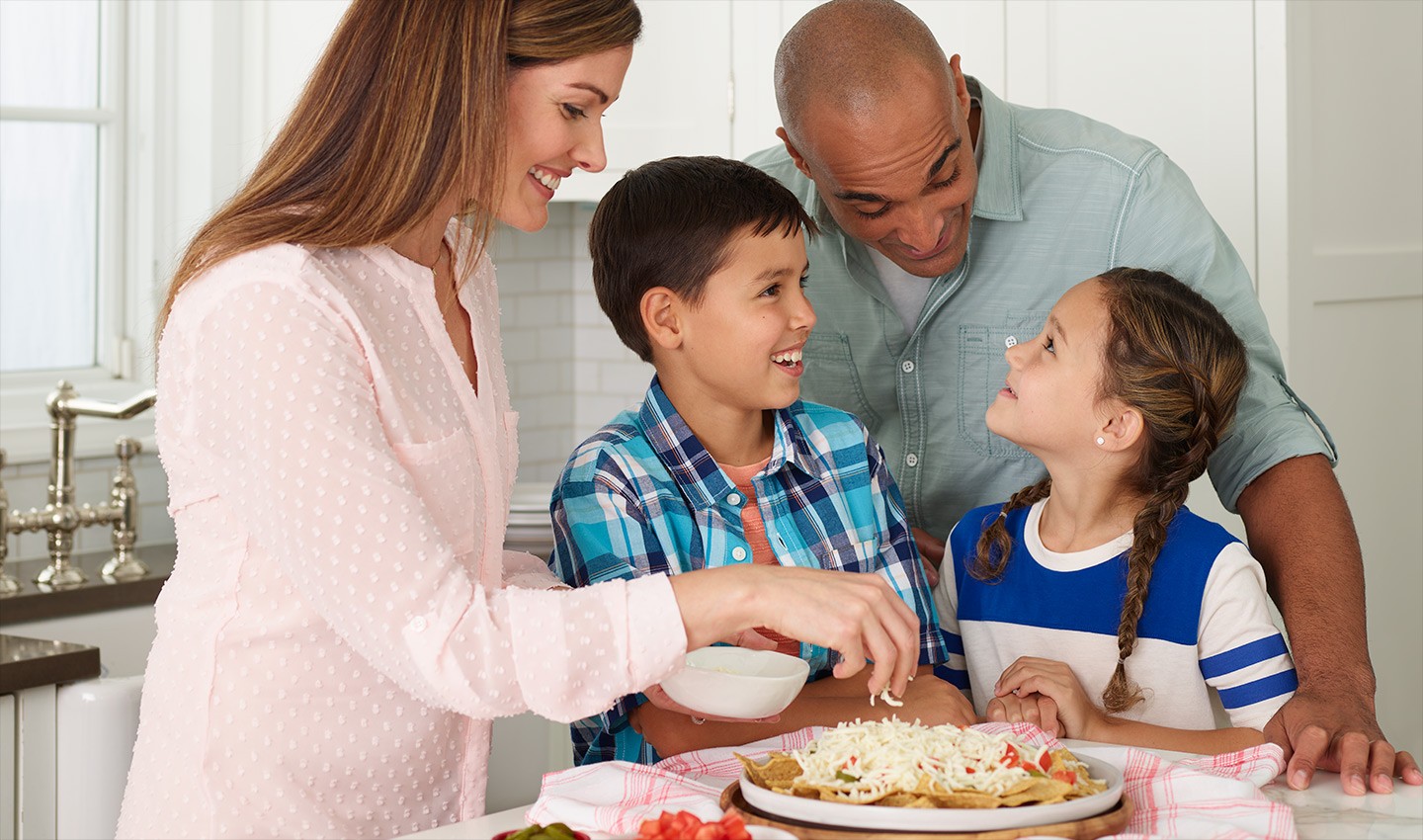 Family of four in kitchen preparing food.